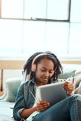 Image showing Tablet, headphones and black girl on the sofa to relax while listening to music, radio or podcast. Rest, technology and African child watching a video or movie on mobile device in living room at home