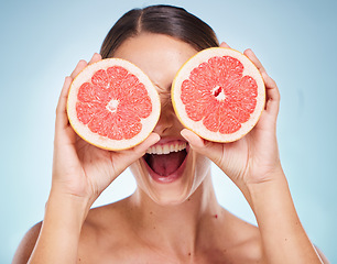 Image showing Face, beauty skincare and woman with grapefruit in studio isolated on a blue background. Organic cosmetics, healthy diet and happy female model holding fruit for vitamin c, facial care and wellness.