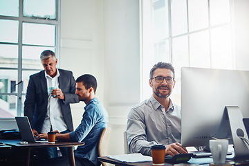 Image showing Computer, portrait and businessman with his colleagues speaking in the background in the office. Technology, success and professional male employee working on a corporate project on a pc in workplace