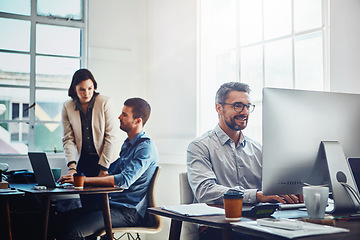 Image showing Office, computer and businessman with his colleagues talking or discussing in the background. Pc, success and mature professional male employee working on a corporate company report in the workplace.