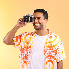 Image showing Photographer, camera and man taking pictures in studio isolated on an orange background. Travel, vacation and male model holding camcorder technology for taking photo for happy memory on holiday.