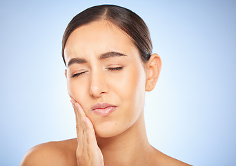 Image showing Toothache, pain and cavity with a model woman holding her mouth in studio on a blue background for oral care. Dental hygiene, plaque and face with an attractive young female rubbing her sore cheek