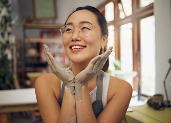 Image showing Hands, face and dirty with an asian woman pottery professional sitting in her studio or workshop. Art, design and creative with a female designer or potter working in her clay or ceramics startup