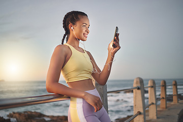 Image showing Fitness, beach and woman with smartphone after running at sunset, online and streaming music or podcast in nature for exercise. Runner, relax and scroll social media after run, smile with earphones.