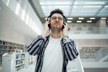 Image showing Student, library and man with music headphones in university, college or school. Thinking, education scholarship and face of young male streaming educational podcast, radio or song, audio or album.