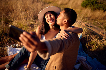 Image showing Couple kiss in selfie with hug, outdoor and picnic in nature, love with smartphone, technology and happy together. Phone for photography, man and woman smile in picture with travel and summer date