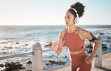 Image showing Black woman, fitness and running with headphones at the beach on sea point in Cape Town for exercise. Sporty African American female runner by the ocean coast having a run for cardio training workout