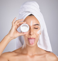 Image showing Woman, skincare cream and tongue in studio for wellness, health and cosmetic health with towel by background. Young healthy model, lotion and funny face for facial, self care and comic by backdrop