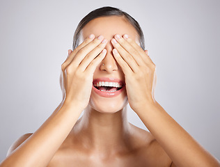 Image showing Woman, hands and covering eyes with smile in satisfaction for skincare, cosmetics or beauty against a grey studio background. Happy female model smiling with covered face for makeup surprise