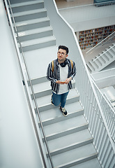 Image showing Library, staircase and student man walking in a education, learning and school research building. College learning, study and bookshelf of person walking down stairs looking at books for information