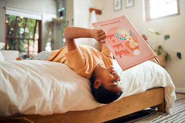 Image showing Happy child reading book on bed for home learning, language education and creative development upside down. Smart, intelligent and Indian kid with English story for fun, relax and holiday activity