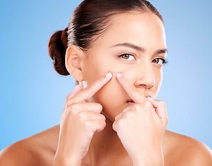 Image showing Woman, face and squeeze pimples, acne and facial scar on studio blue background. Portrait of young female model worried for skincare problem, aesthetic beauty cosmetics and pop blackhead with fingers