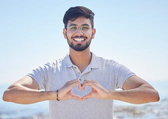 Image showing Beach portrait and a man heart hand for summer holiday freedom, happiness and wellness. Happy Indian person enjoying ocean sun with love shape and optimistic smile for travel adventure.