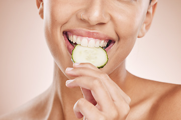 Image showing Hand, mouth and cucumber with a model black woman biting a vegetable in studio on a beige background. Health, beauty and skincare with a young female eating a slice of veg for natural wellness