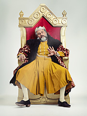 Image showing King, royalty and bored man on throne in studio isolated on gray background. Monarch, medieval royal and annoyed senior male, leader or frustrated ruler, looking at hand and sitting on golden seat.