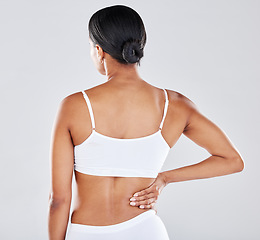 Image showing Back, body and pain with a model black woman holding her side in studio on a gray background while suffering from injury. Medical, health and anatomy with a female in underwear rubbing her muscle