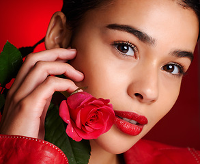 Image showing Portrait, beauty and red rose with a model woman holding a flower in studio on a wall background for valentines day. Face, romance and love with an attractive young female posing to promote dating