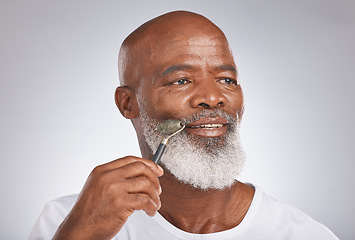 Image showing Senior black man, skincare and facial roller to massage skin during self care for wellness, dermatology and cosmetics. Headshot of male with beauty tool on grey studio background for a spa treatment