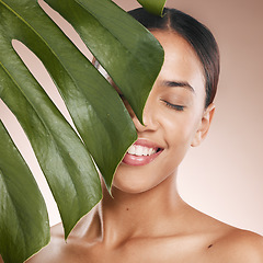 Image showing Black woman, smile and leaf with beauty, studio and cosmetic wellness with smile, face glow and makeup. Model, skin health and facial cosmetics, self care and aesthetic with leaves by studio backdrop