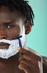 Image showing Black man, shaving and studio with skincare foam, razor and facial cosmetics for beauty by blue background. African gen z model, hair removal cream and shave for aesthetic, cleaning and face grooming