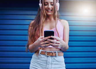 Image showing Social media, music and woman reading on a phone with a podcast, communication and app in the city. Headphones, radio and girl typing on a mobile, streaming audio and sound on a blue wall in Germany