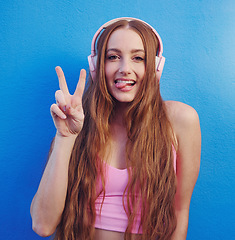 Image showing Music, peace and tongue with the portrait of a woman on a blue background while listening to the radio. Face, hand and headphones with an attractive young female streaming an audio playlist or song