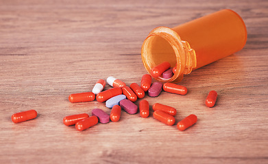 Image showing Pills, medicine and suicide with a tablet container on a wooden table or surface for drug addiction and overdose. Health, medication and pharmacy with prescription tablets spilled from above