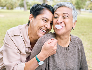 Image showing Senior women, friends and hug in park for comic, funny and happy time together in nature with bubblegum. Old woman, embrace and laughing for memory, joke or bubble by trees, nature or forest to relax