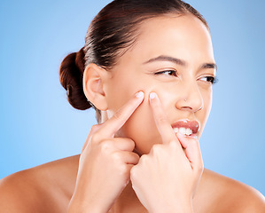 Image showing Skincare, beauty and woman squeeze pimple before a natural cosmetic face treatment in a studio. Acne, cosmetics and female model pop blackheads or facial scar with her fingers by a blue background.