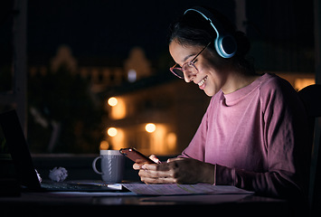 Image showing Phone, night and woman networking with headphones while listening to music, radio or podcast. Happy, smile and girl browsing social media, mobile app or internet with cellphone at a desk in her home.