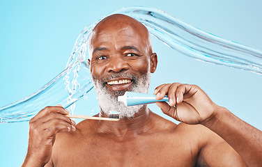 Image showing Water splash, oral hygiene and portrait of a man in a studio for mouth health and wellness. Toothpaste, toothbrush and elderly African guy brushing his teeth for fresh dental care by blue background.