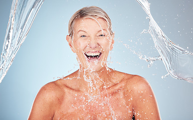 Image showing Skincare, senior and portrait of a woman with a water splash isolated on a blue background. Self care, happy and face of an excited elderly model cleaning her body for wellness on a studio backdrop