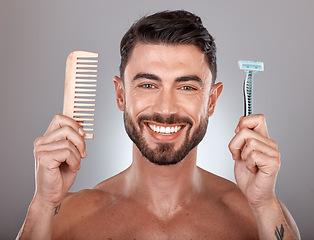 Image showing Portrait, shaving and comb with a man model holding a razor in studio on a gray background for skincare. Face, wellness and hands with a handsome young male in the bathroom to shave his beard