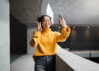 Image showing Woman, peace and selfie in office building, smile and happy while on internet, pose and emoji. Asian, girl and business entrepreneur with smartphone for photo, peace sign and hand for profile picture