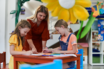 Image showing Creative kids during an art class in a daycare center or elementary school classroom drawing with female teacher.