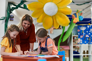 Image showing Creative kids during an art class in a daycare center or elementary school classroom drawing with female teacher.