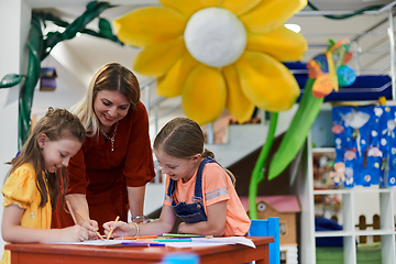 Image showing Creative kids during an art class in a daycare center or elementary school classroom drawing with female teacher.