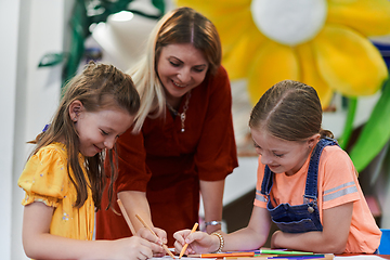 Image showing Creative kids during an art class in a daycare center or elementary school classroom drawing with female teacher.