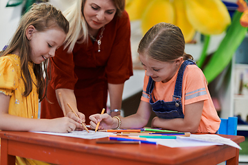 Image showing Creative kids during an art class in a daycare center or elementary school classroom drawing with female teacher.