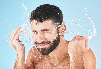 Image showing Man, cleaning and beauty with splash in studio for health, self care and smile by blue background. Model, skincare and water with clean for healthy facial, self love and cosmetics by studio backdrop