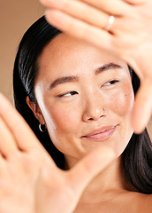 Image showing Asian woman, hand frame and studio for skincare, natural skin glow and smile with cosmetics for health. Japanese model, cosmetic beauty and healthy aesthetic for self care, wellness or happy headshot