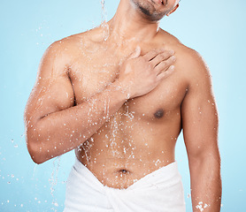 Image showing Body, water and shower with a man model standing in studio on a blue background for hygiene or hydration. Splash, health and wellness with a male wearing a towel in the bathroom after bathing