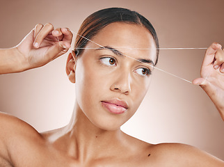 Image showing Eyebrows, cosmetics and woman threading hair for grooming, body health and salon treatment on a studio background. Beauty, shaping and cosmetic model with thread for brow trimming and facial care