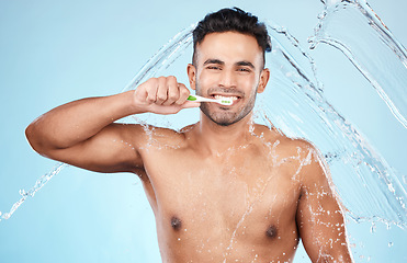 Image showing Face, water splash and man with toothbrush for cleaning in studio on blue background. Dental veneers, hygiene and portrait of happy male model brushing teeth for oral wellness, health or fresh breath