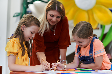 Image showing Creative kids during an art class in a daycare center or elementary school classroom drawing with female teacher.