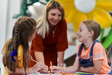 Image showing Creative kids during an art class in a daycare center or elementary school classroom drawing with female teacher.