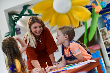 Image showing Creative kids during an art class in a daycare center or elementary school classroom drawing with female teacher.