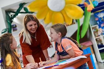 Image showing Creative kids during an art class in a daycare center or elementary school classroom drawing with female teacher.