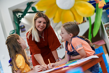 Image showing Creative kids during an art class in a daycare center or elementary school classroom drawing with female teacher.