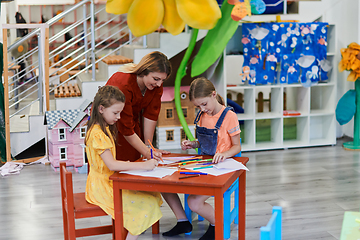 Image showing Creative kids during an art class in a daycare center or elementary school classroom drawing with female teacher.